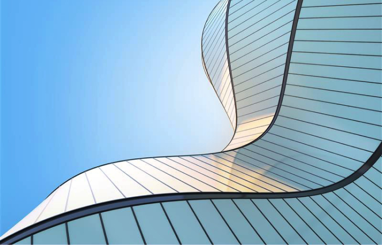 A modern building featuring a sleek, curved glass facade reflecting sunlight against a deep blue sky