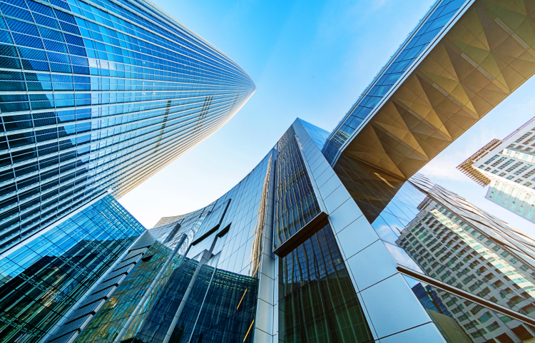 An upward view of glimmering modern skyscrapers against a clear blue sky